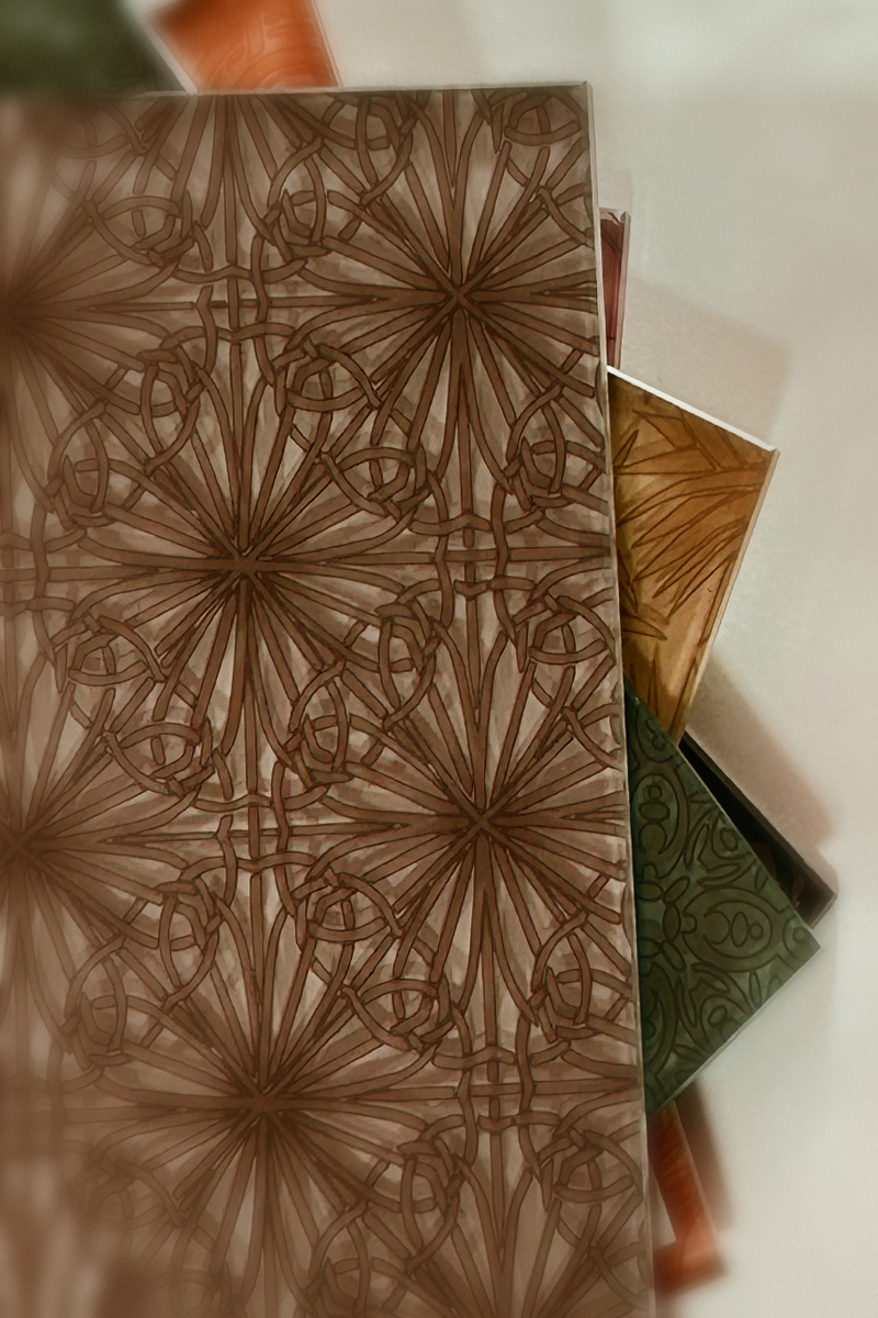 Still life of back-painted decorative glass samples in ink, warm bronze, and moss green beside a reeded glass sample, with a live-oak leaf and Spanish moss on a warm walnut surface