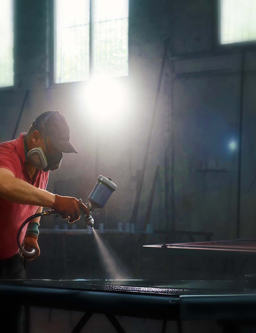 Spray gun held in hand with pigment jars in the background, small to mid fabricator shop